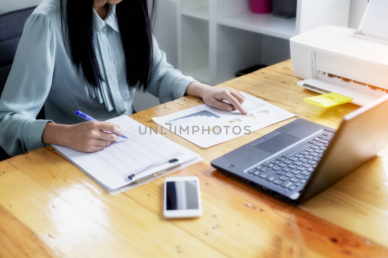 Beautiful young businesswoman doing some paperwork while sitting at office desk in front of computer.