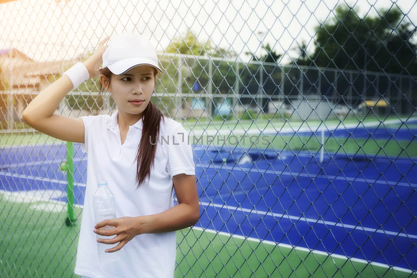 Beautiful young woman drinking water on the tennis court after playing tennis to exercise. Health Care Concept