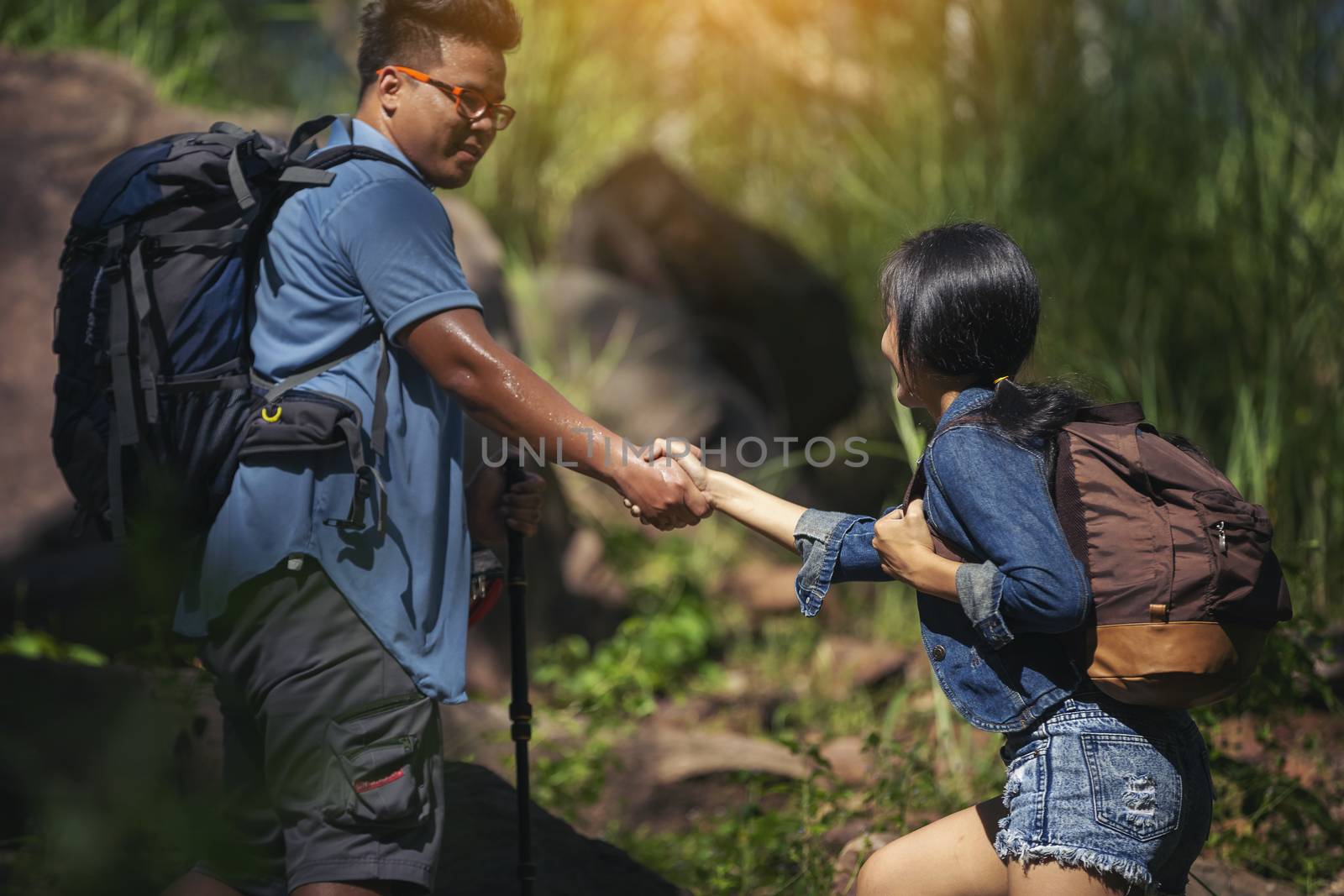 Couples help by pulling their hands together in hiking for tourism. Young man helps his girlfriend climbing for a trip.