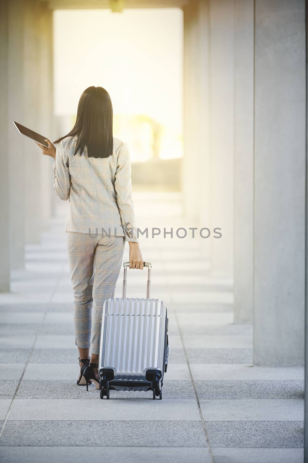 Portrait of business woman looking digital tablet with white travel bag on walkway while waiting to travel to the destination 