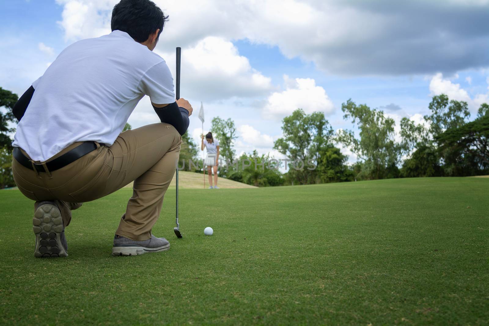 Golf player check line for putting golf ball on green grass. Golf player crouching and study the green before putting shot