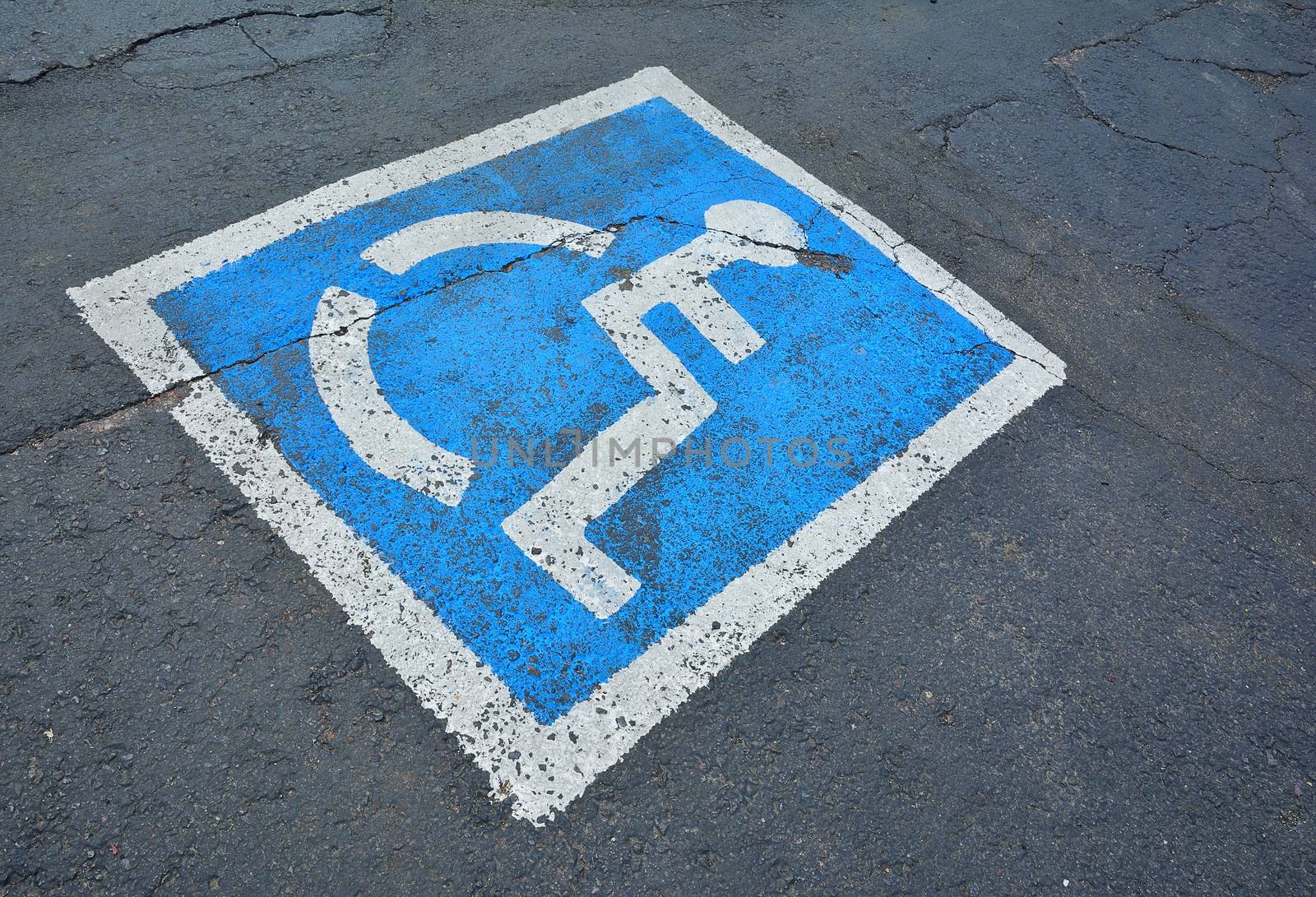 Disabled blue parking sign painted on dark asphalt.