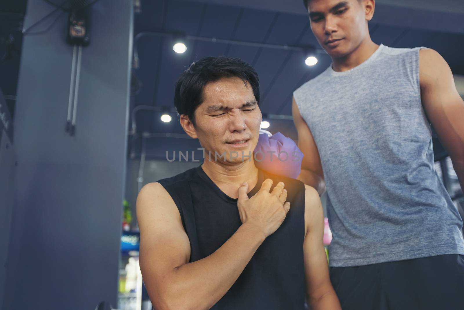 Handsome young man who is feeling pain from exercise and received an ice pack from his friend to relieve the pain