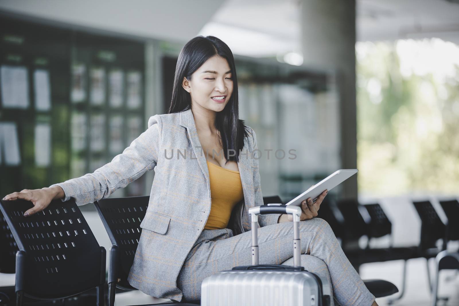 Portrait of business woman looking digital tablet with white travel bag While waiting to travel to the destination 
