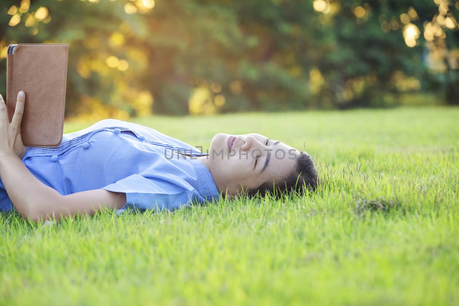 Portrait of beautiful young women who relax by watching the tablet in the lawn relax. Smiling Thai woman using digital tablet while lying in green spring garden