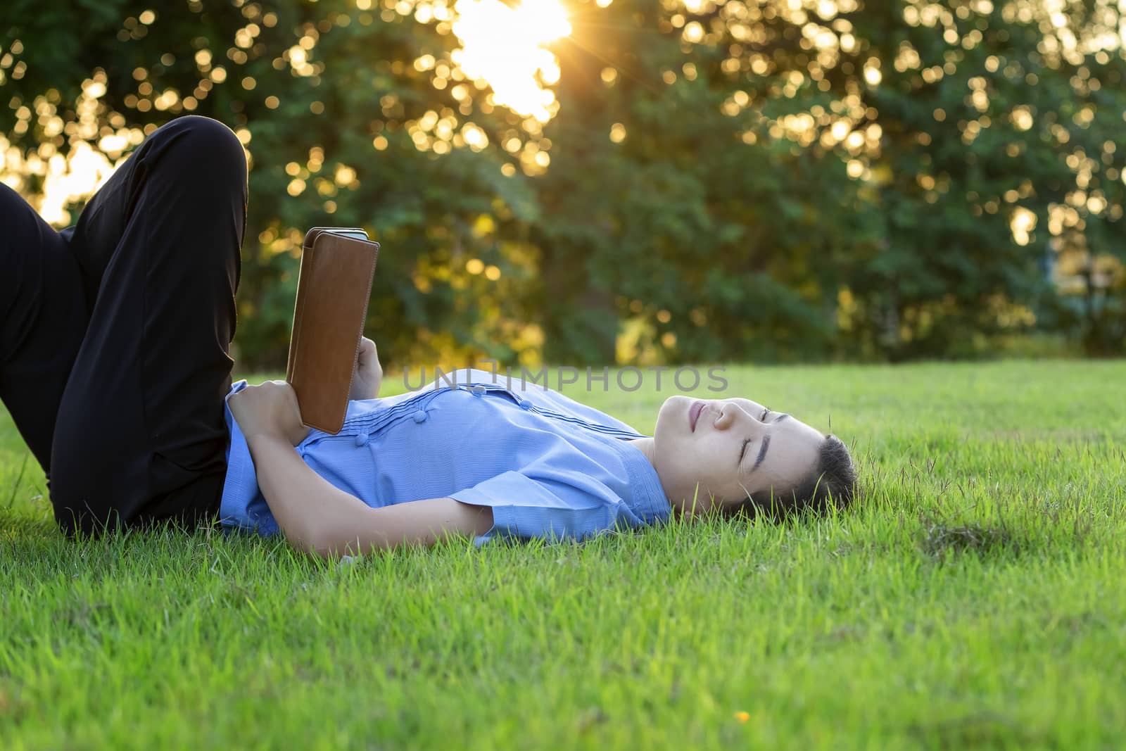 Portrait of beautiful young women who relax by watching the tablet in the lawn relax. Smiling Thai woman using digital tablet while lying in green spring garden