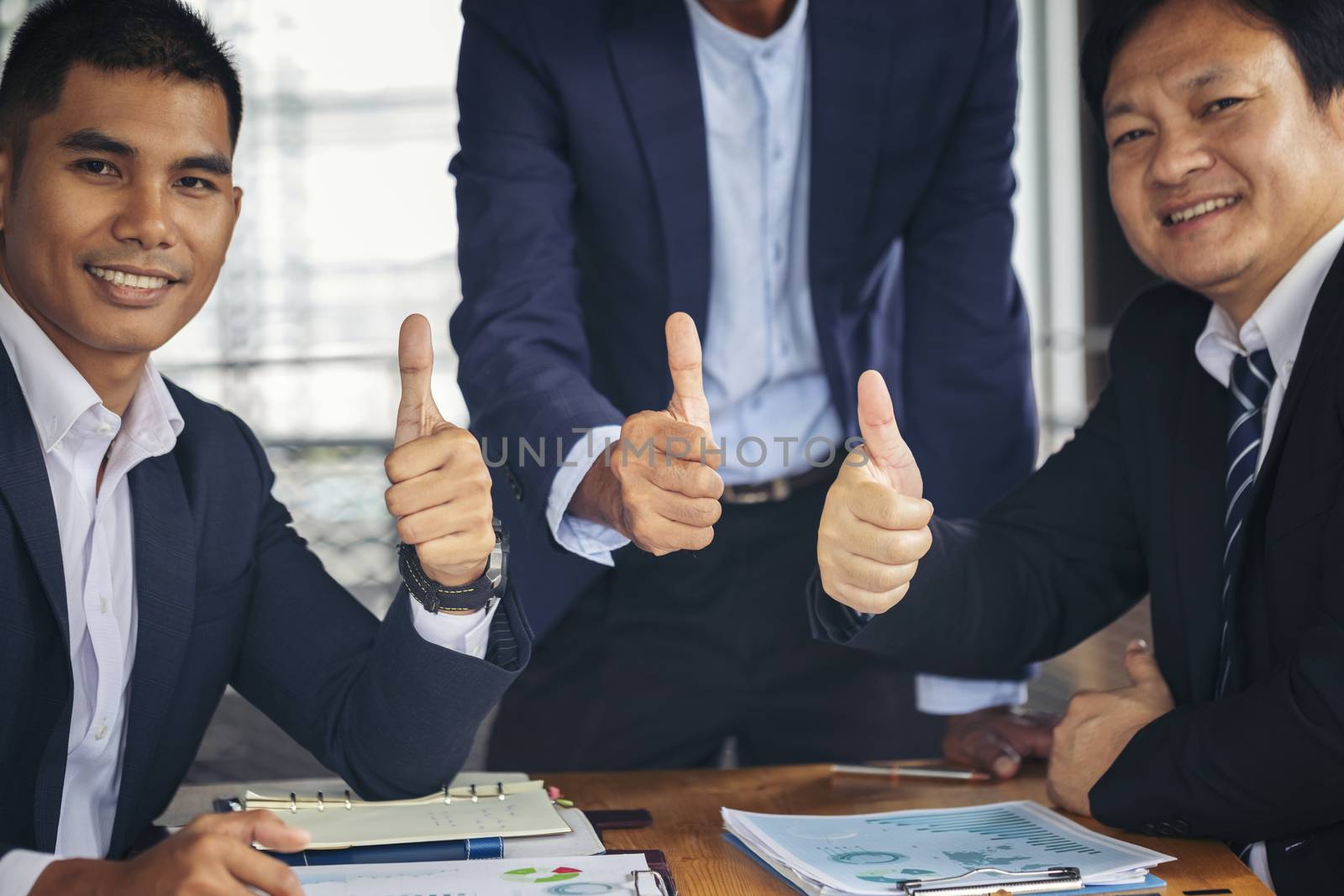 Three business partners keeping thumbs up. cheerful business group giving thumbs up