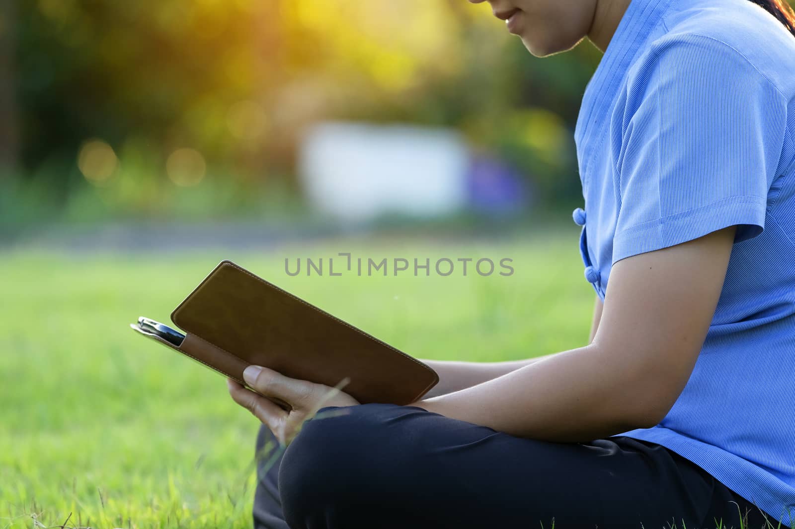 Portrait of beautiful young women who relax by watching the tablet in the lawn relax. Smiling Thai woman using digital tablet while lying in green spring garden