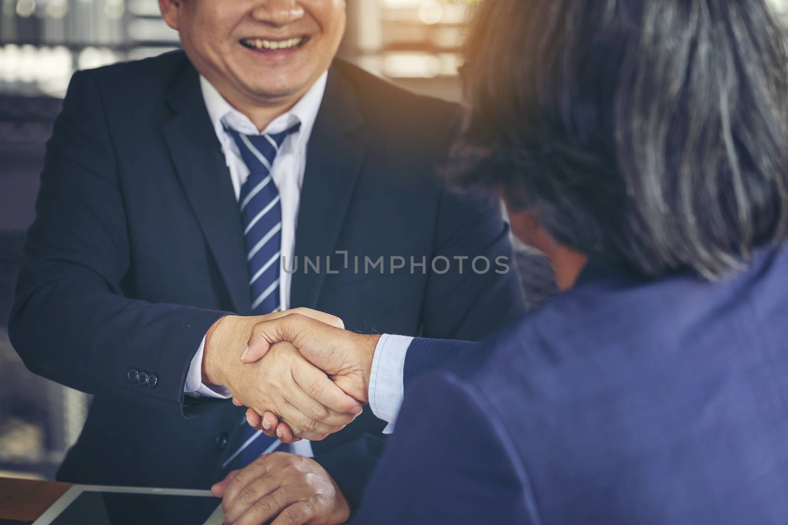 Young business people shaking hands in the office. Finishing successful meeting. Businessman holding pens and holding graph paper are meeting to plan sales to meet targets set in next year.