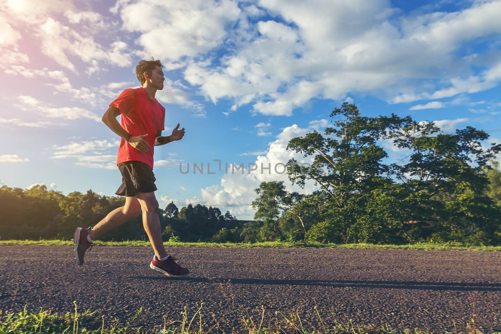 Handsome young man runs for good health on a rural road that is full of forests and beautiful nature.