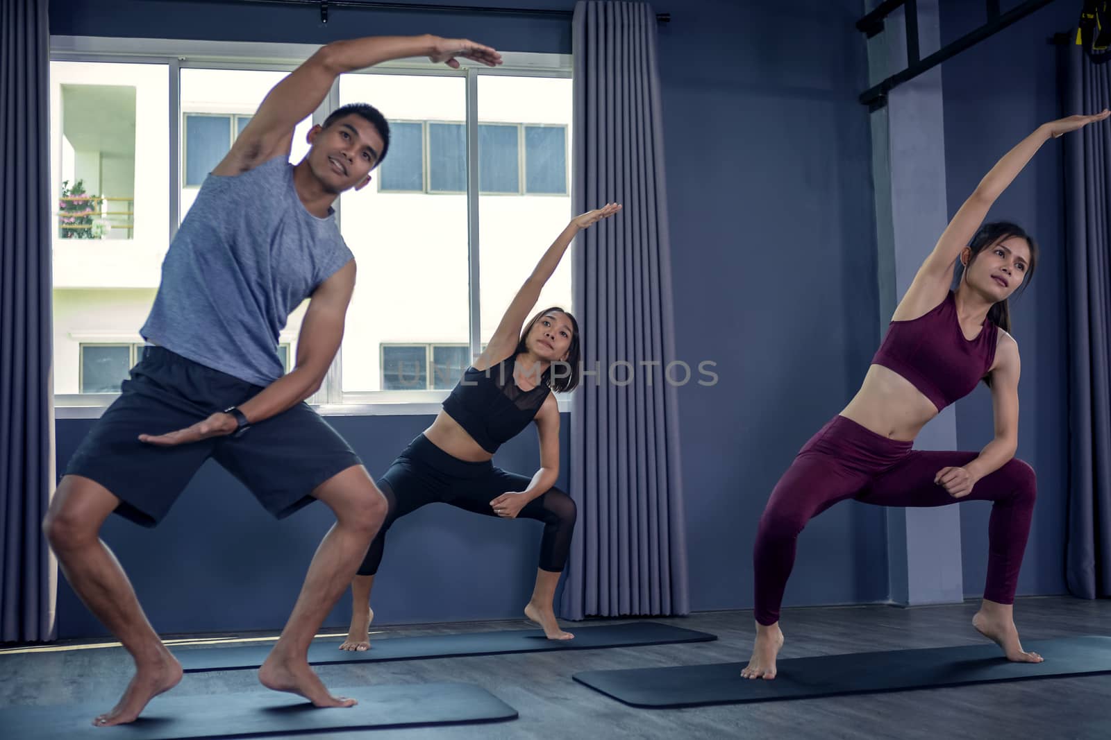 Beautiful woman practicing yoga position and has a close trainer in an indoor gym studio. Healthy and wellness lifestyle concept