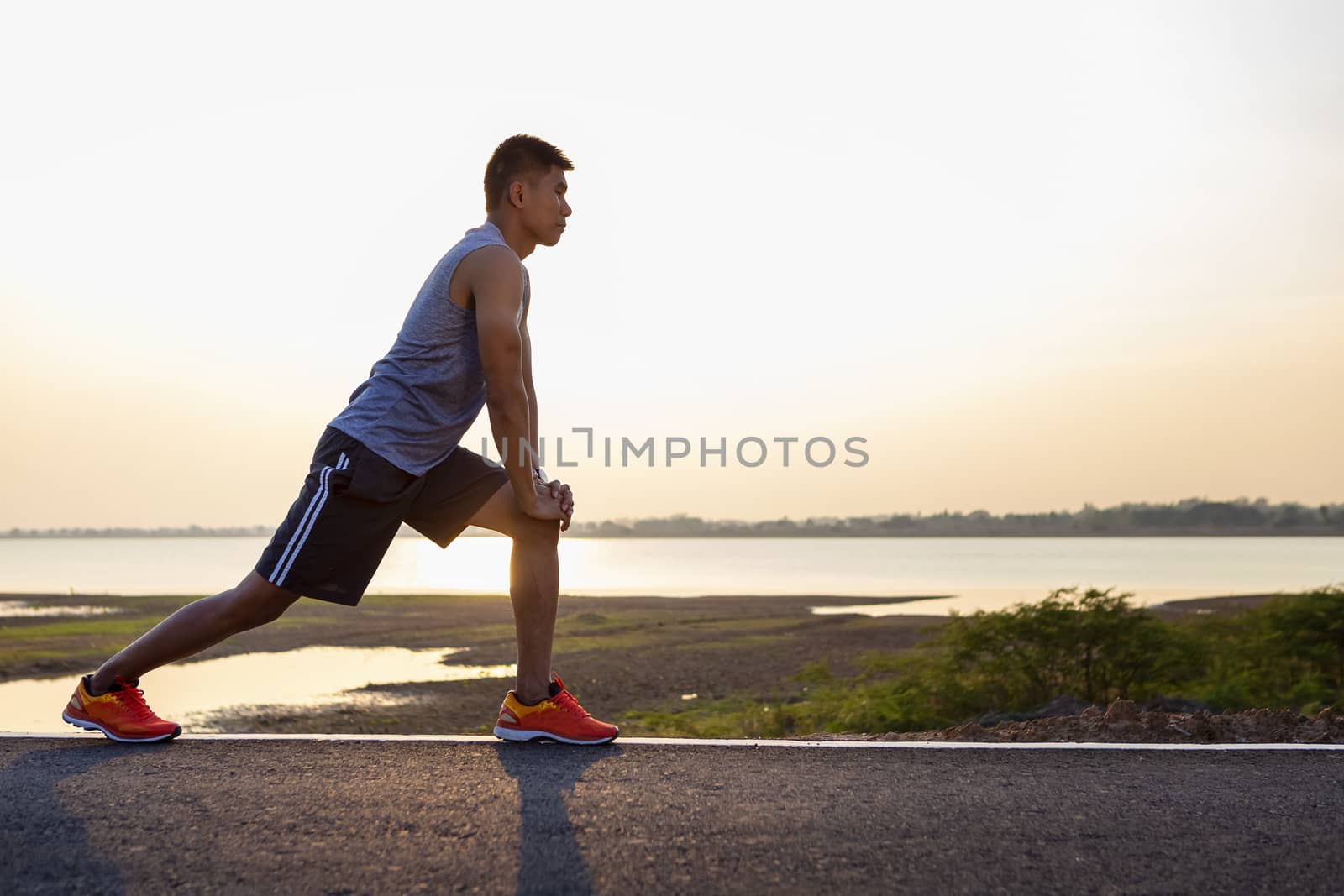 Shot of flexible young man warms up before jogging on the road in the park. People, sport, fitness and flexibility concept