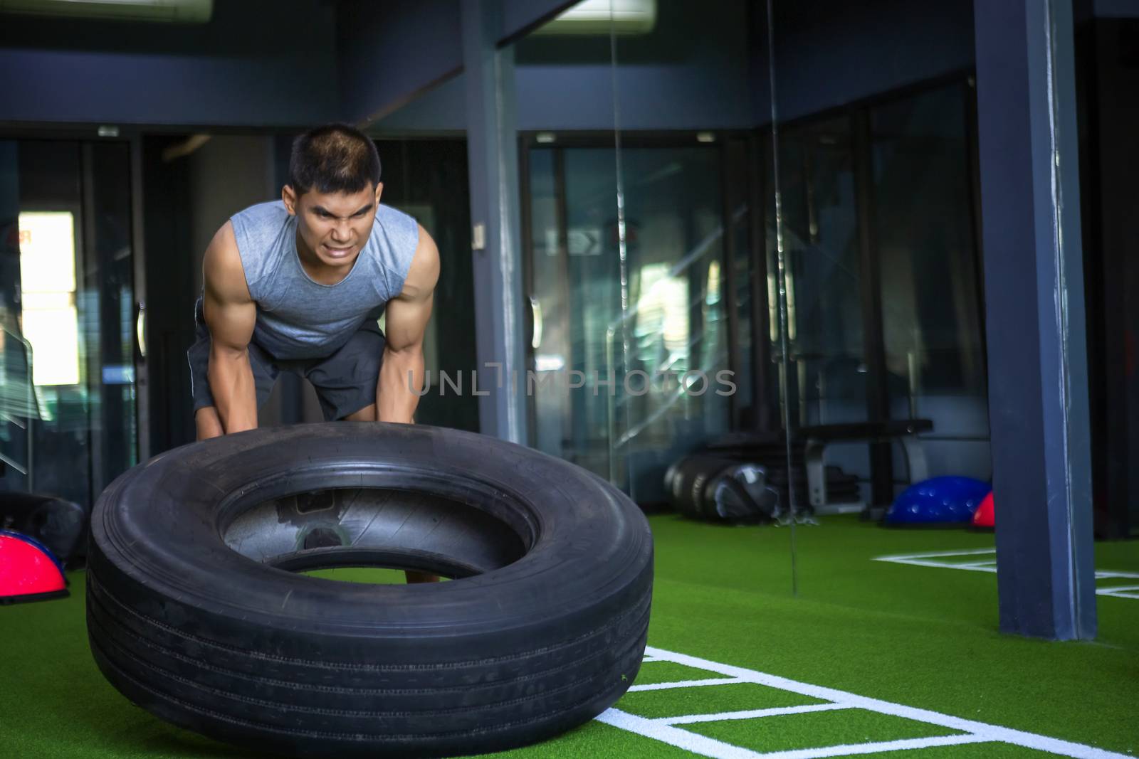 Strong muscular man lifts tire as part of his fitness program. Health fitness concept