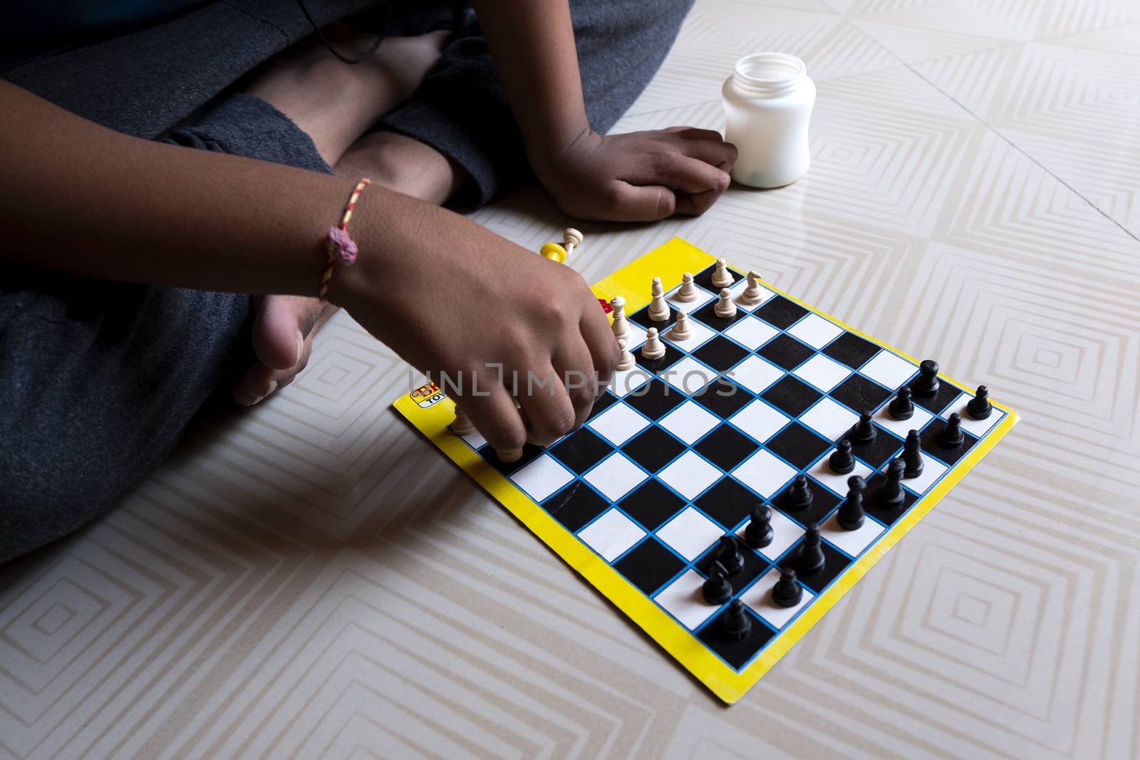 A closeup shot of a person sitting on the white patterned floor and playing chess