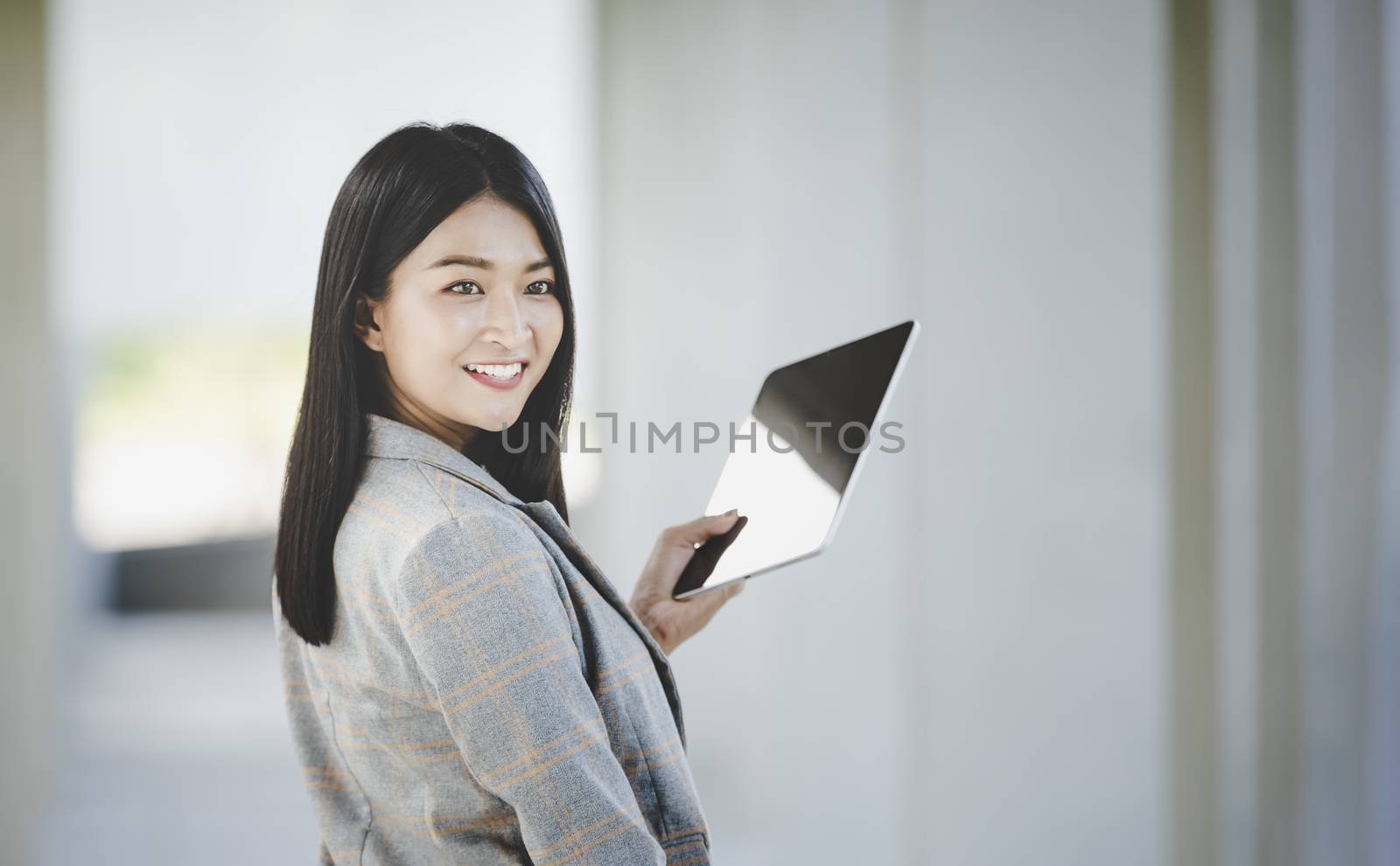 Portrait of business woman looking digital tablet with white travel bag on walkway while waiting to travel to the destination 