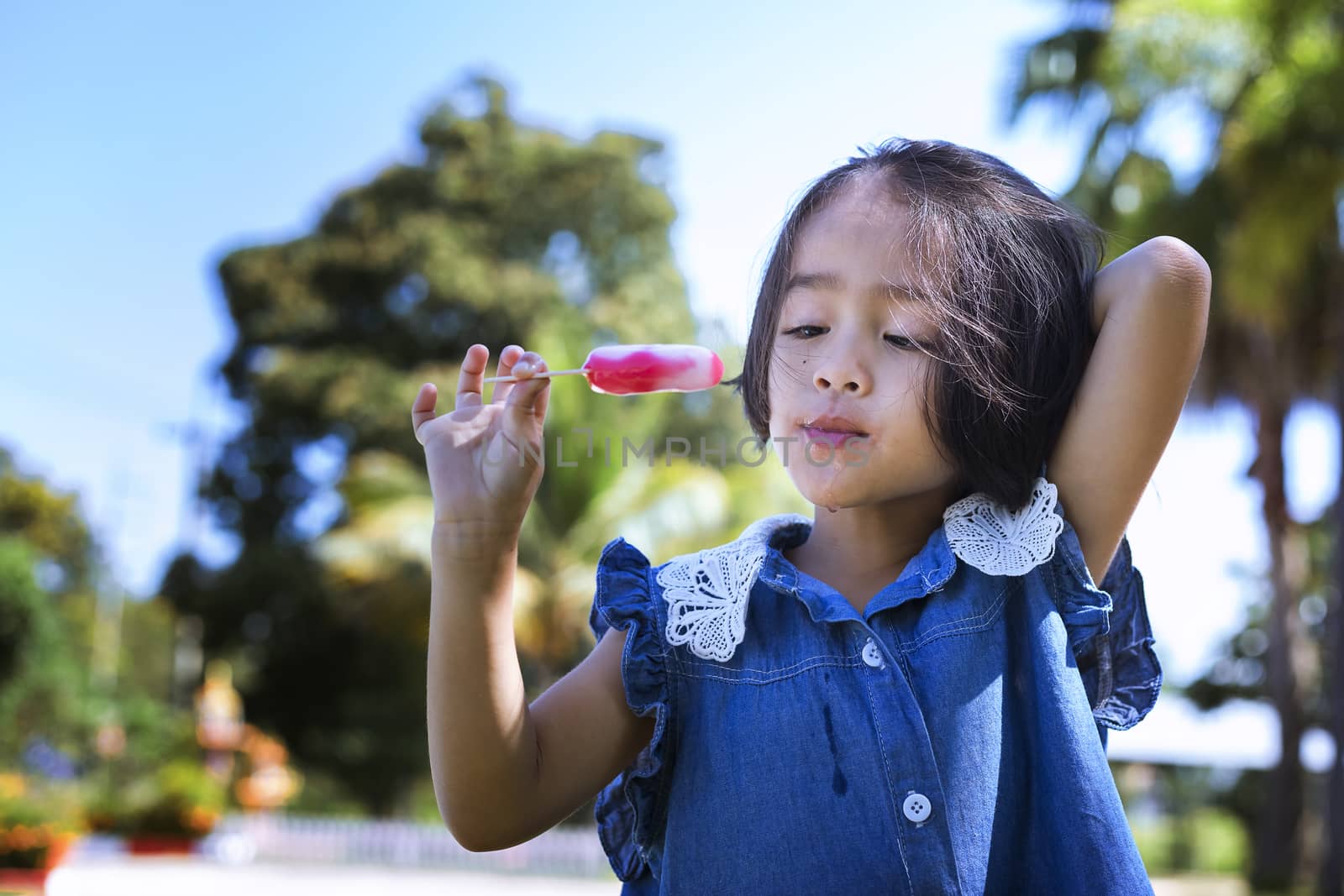 Cute little girl eating popsicle with sunset background