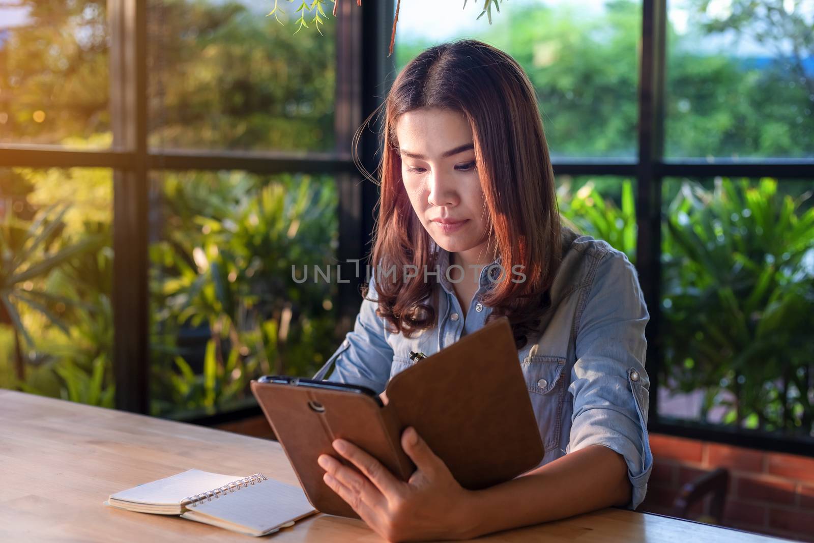 Beautiful Asian businesswoman who uses a tablet in the coffee shop to contact customers and check emails. Business concept