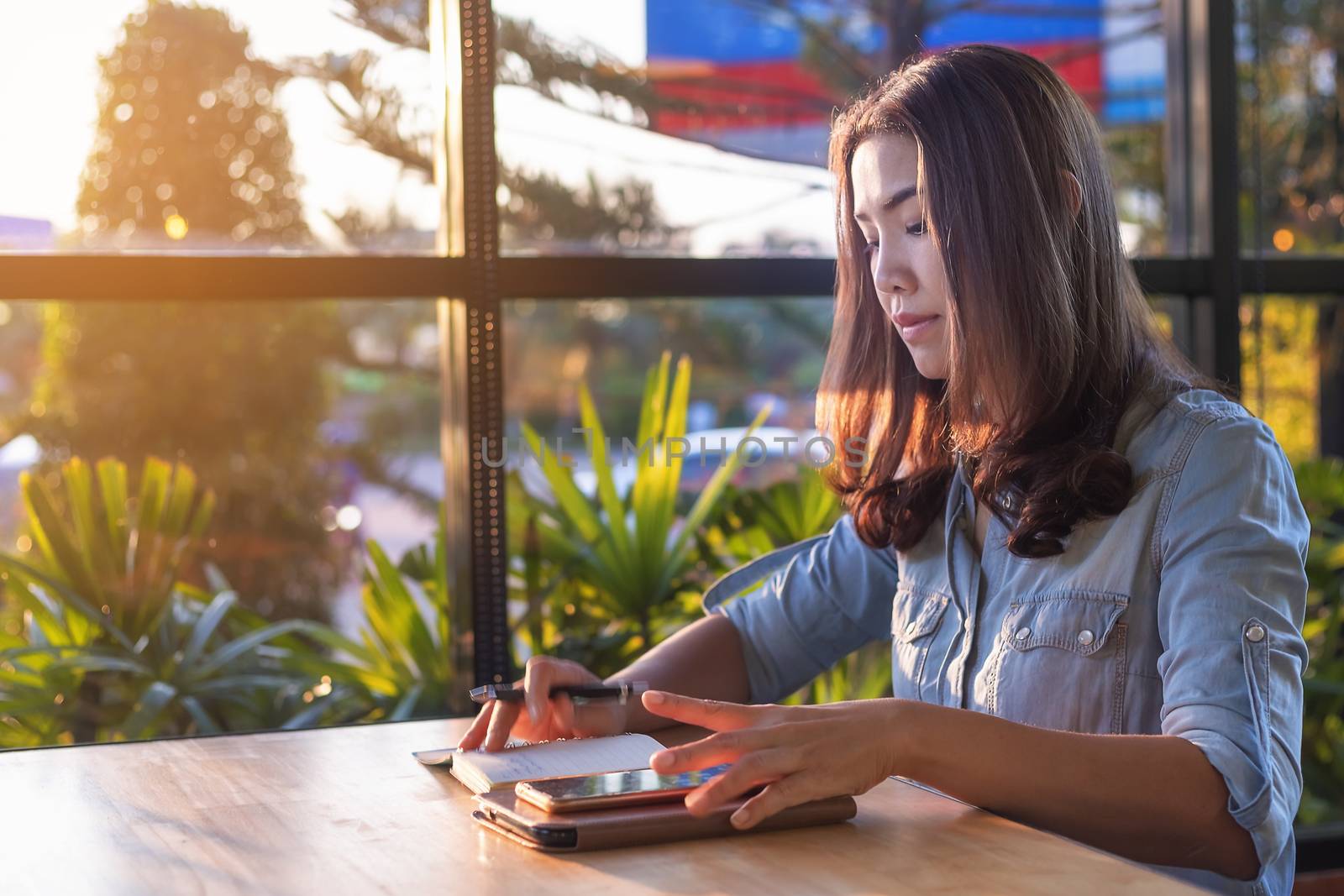 Beautiful Asian businesswoman who uses a tablet in the coffee shop to contact customers and check emails. Business concept