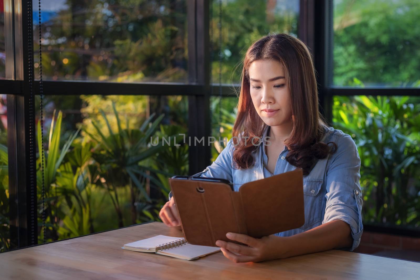 Beautiful Asian businesswoman who uses a tablet in the coffee shop to contact customers and check emails. Business concept