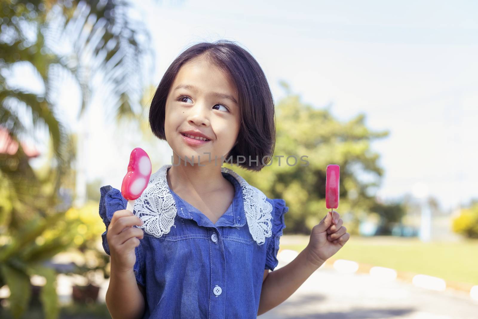 Cute little girl eating popsicle with sunset background