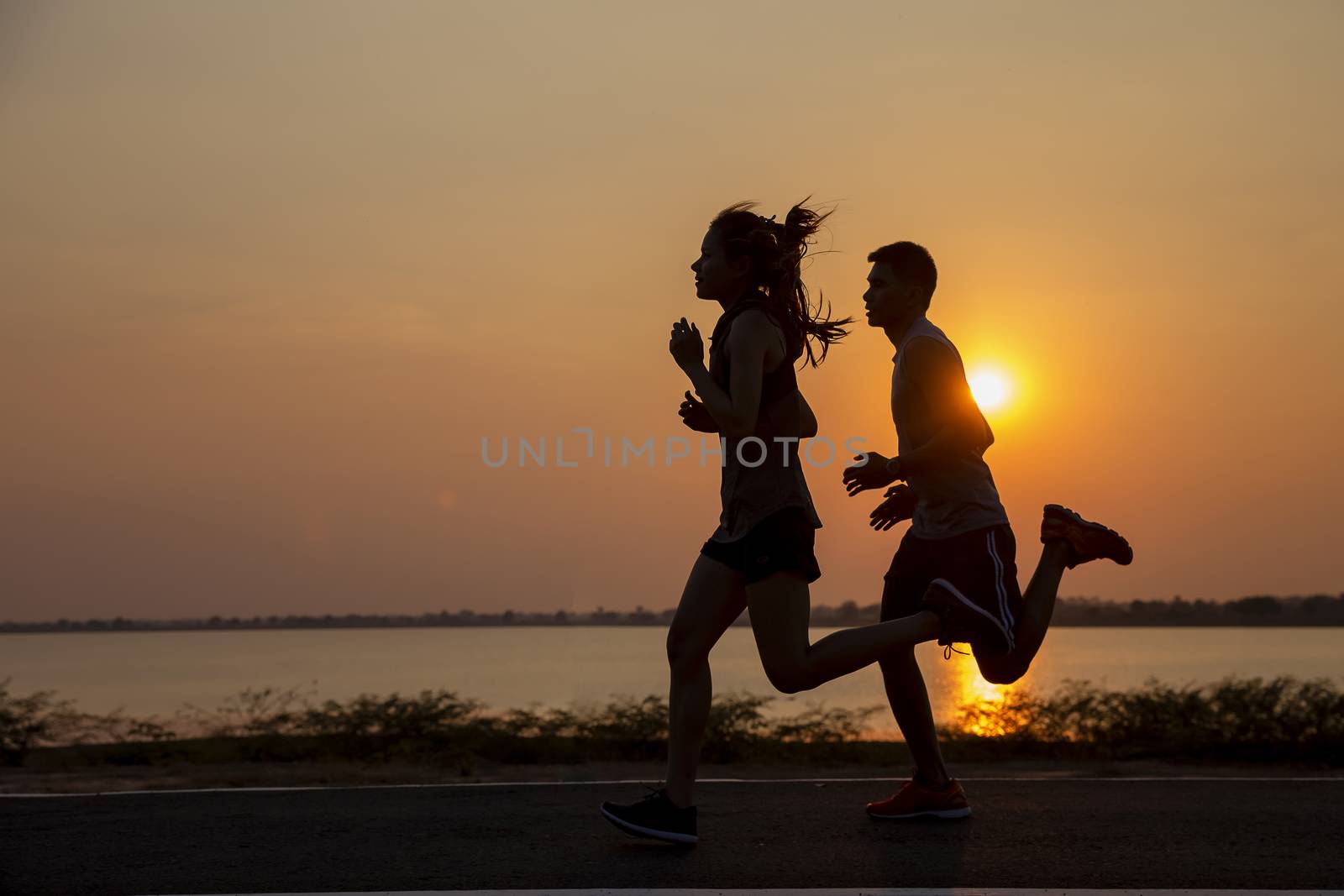 Lovers on the rural road at sunset in summer field. silhouette, running sportsman in the sun, toning. Lifestyle sports background 
