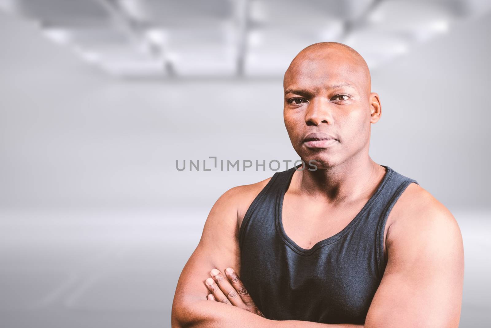 Portrait of bald bodybuilder with arms crossed against white abstract room