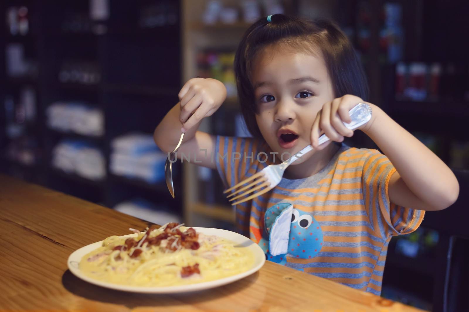 Asian little girl is eating spaghetti bolognese in the restaurant happily.