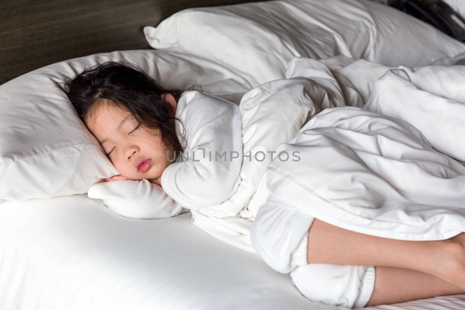 Little girl sleeping in bed with white blanket.