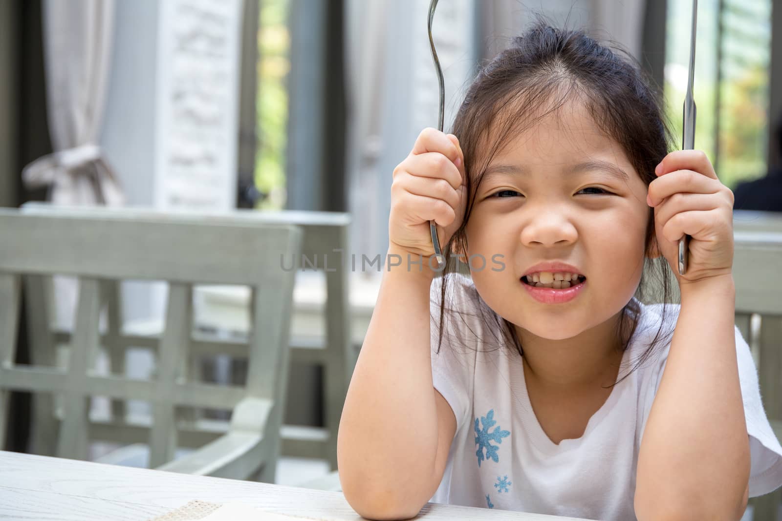 Kid holding spoon and fork in restaurant.