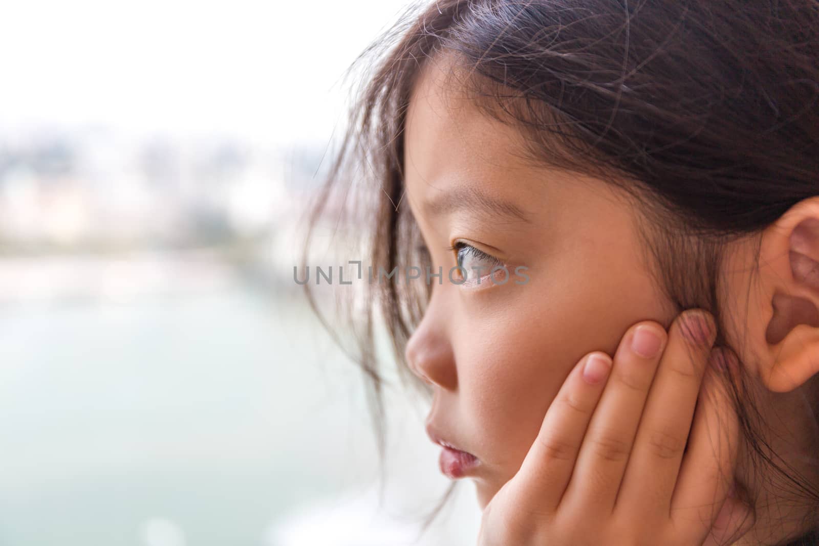 Sad little girl looking out of window waiting for someone.