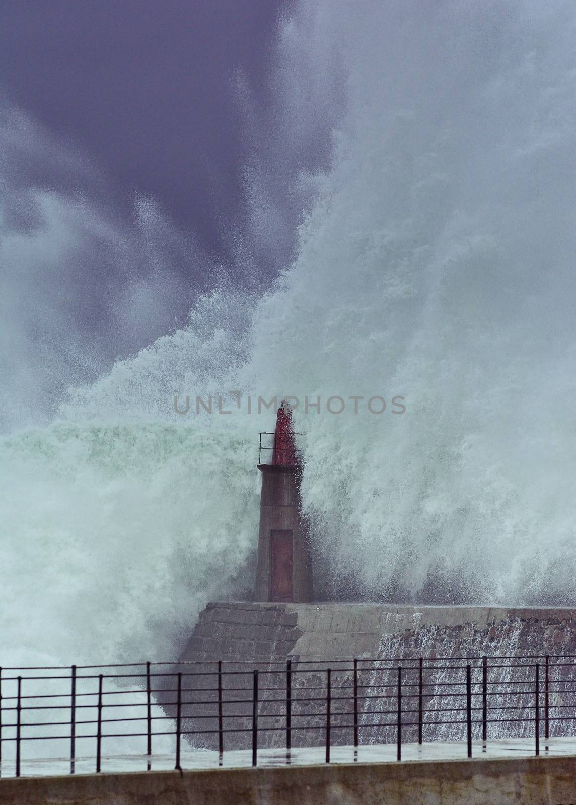 Stormy wave over old lighthouse and pier of Viavelez in Asturias, Spain.