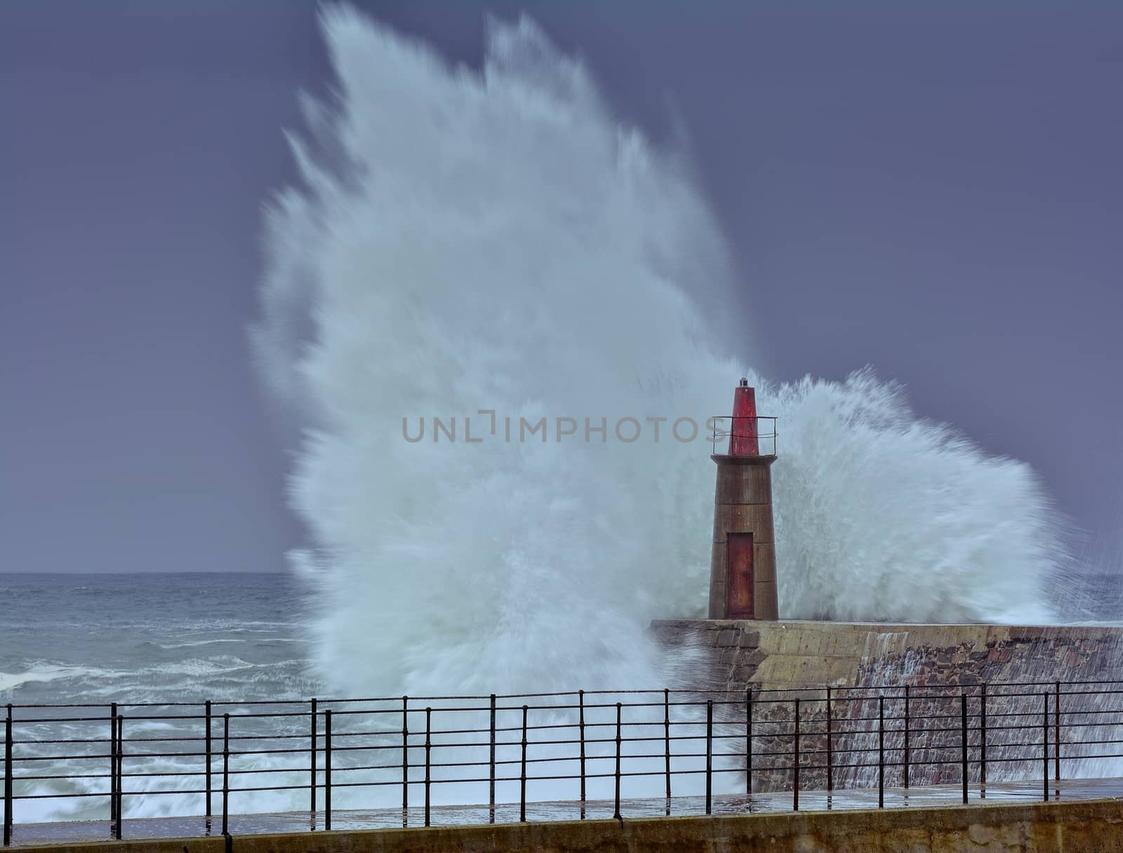 Stormy wave over old lighthouse and pier of Viavelez in Asturias, Spain.