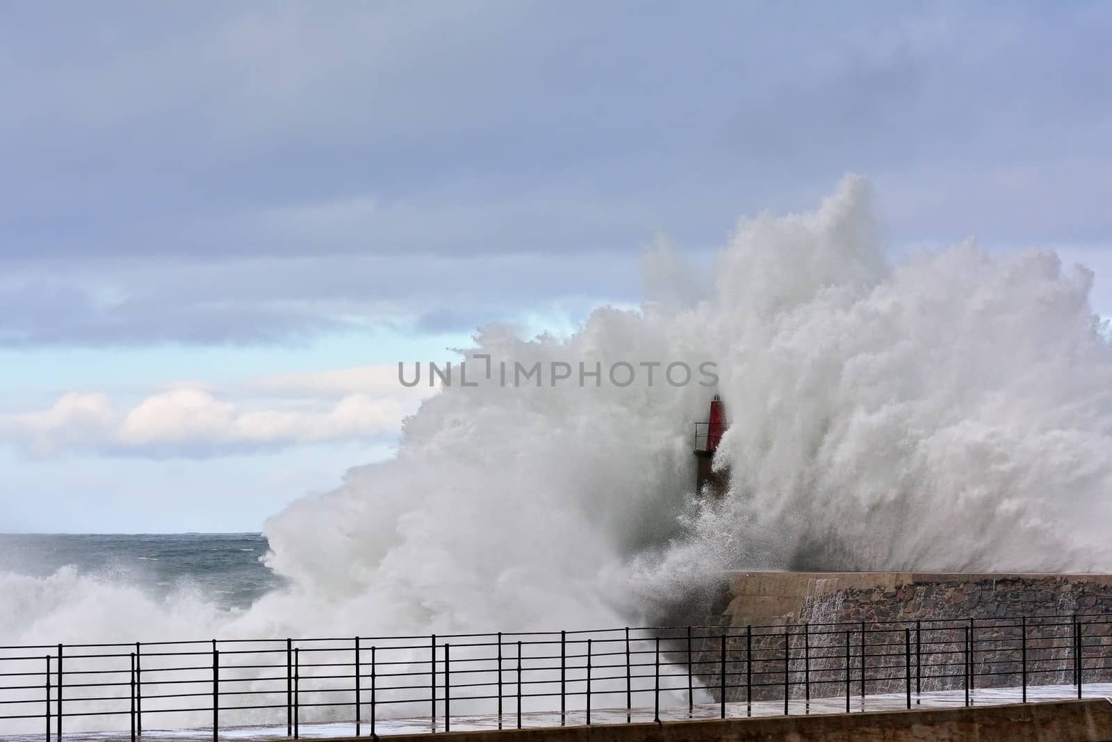 Stormy wave over old lighthouse and pier of Viavelez in Asturias, Spain.