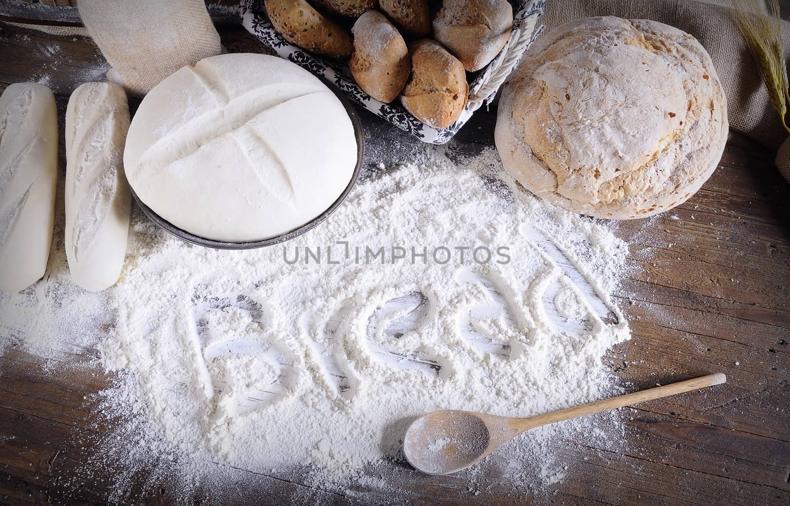 Word 'bread' written on flour scattered on wooden table. Bread making ingredients. From above