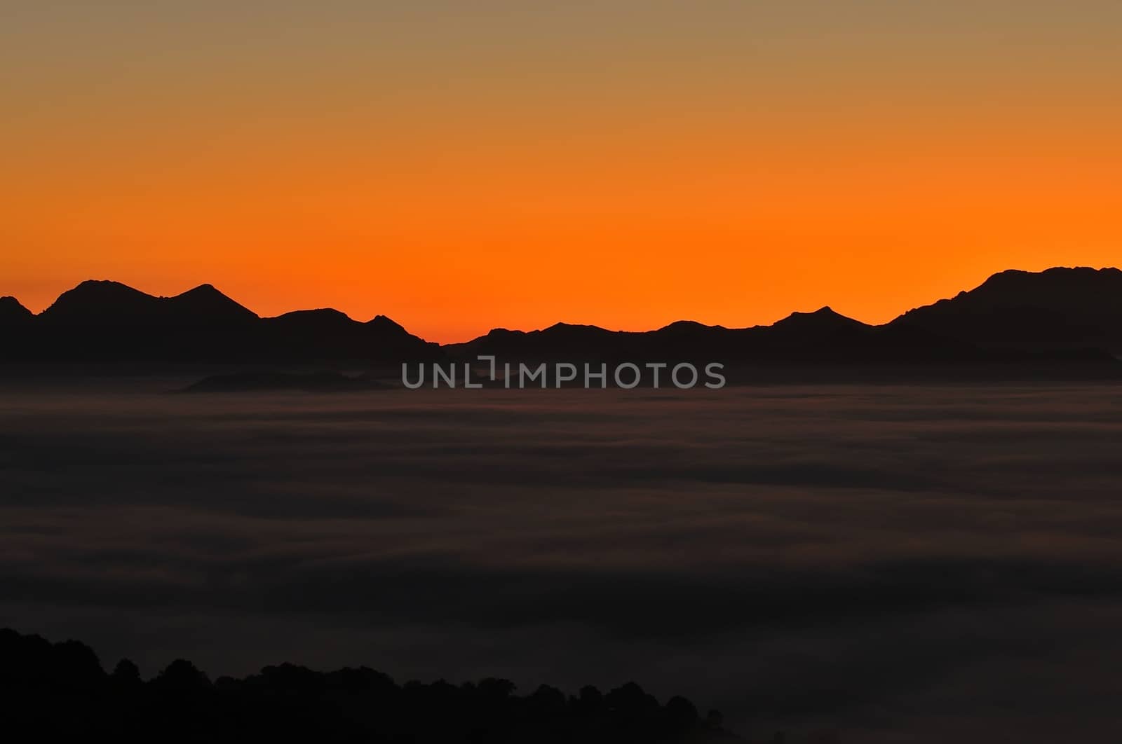 Silhouette of mountains with fog at sunset against of bright vivid sky