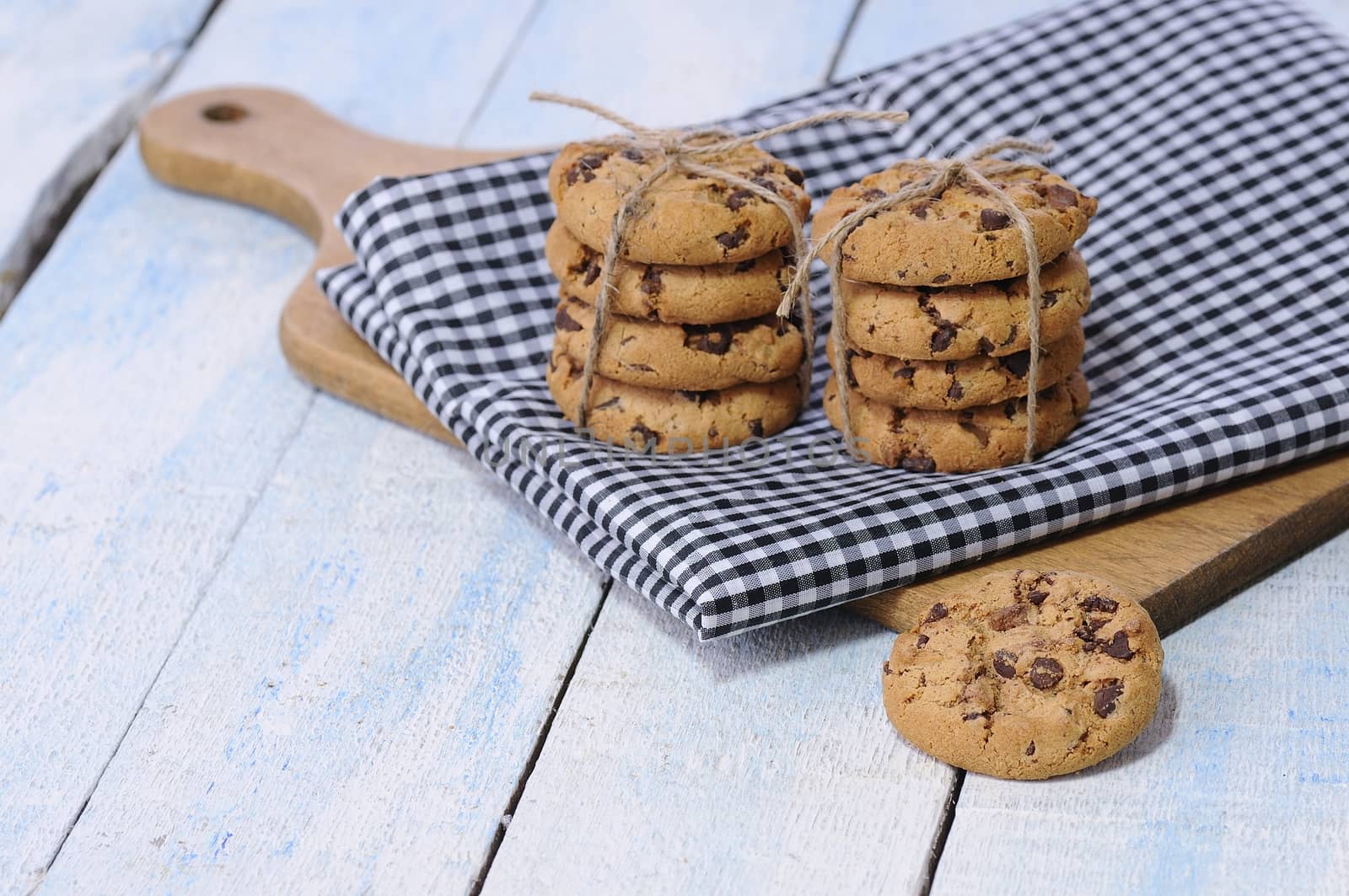 Two stacks of chocolate chip cookies on checked napkin covered wooden board