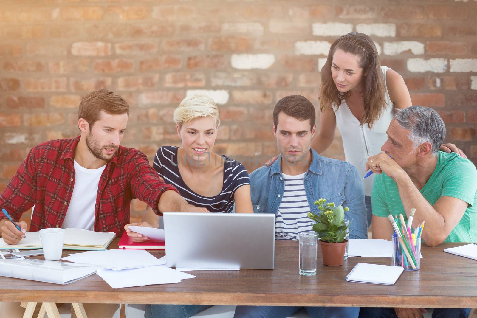 Teamwork using laptop together against brick wall