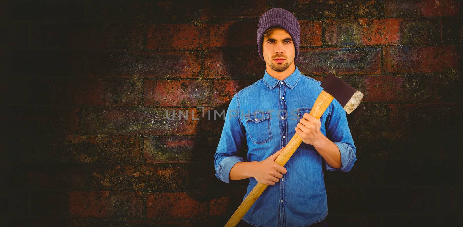 Portrait of serious hipster holding axe against texture of bricks wall
