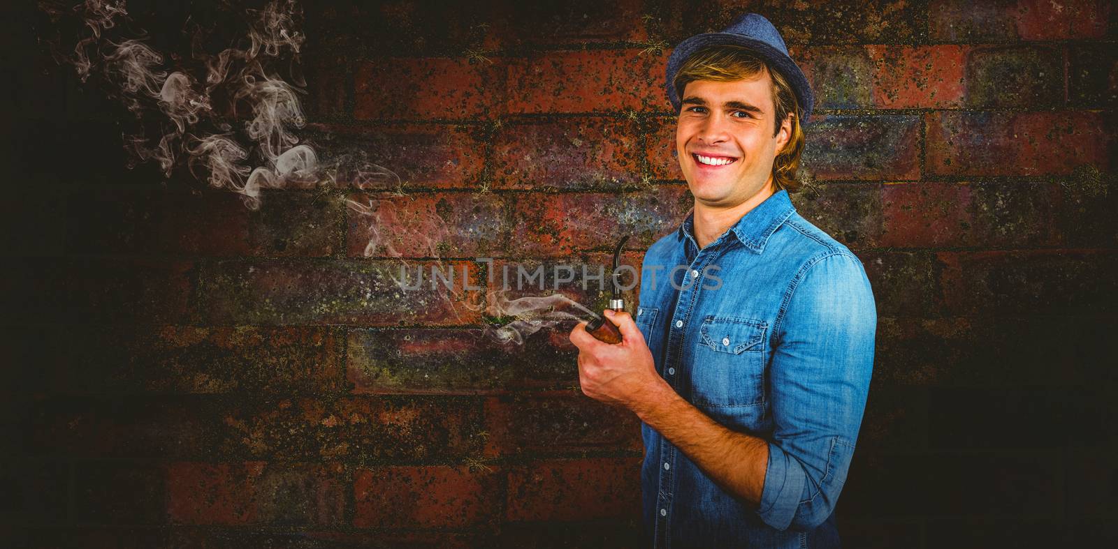 Cheerful hipster holding pipe against texture of bricks wall