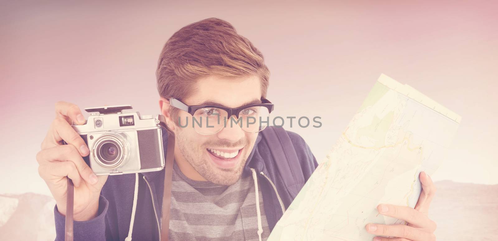 Portrait of happy man holding map and camera against mountain trail