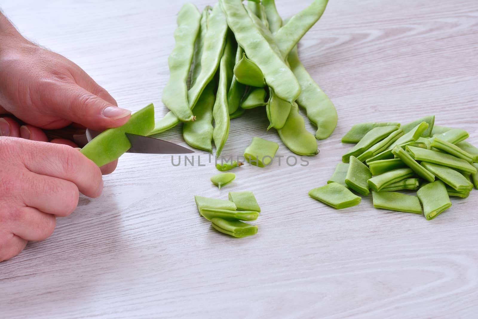 Close-up of man's hands cutting green peas. Mushrooms and sliced bacon on table