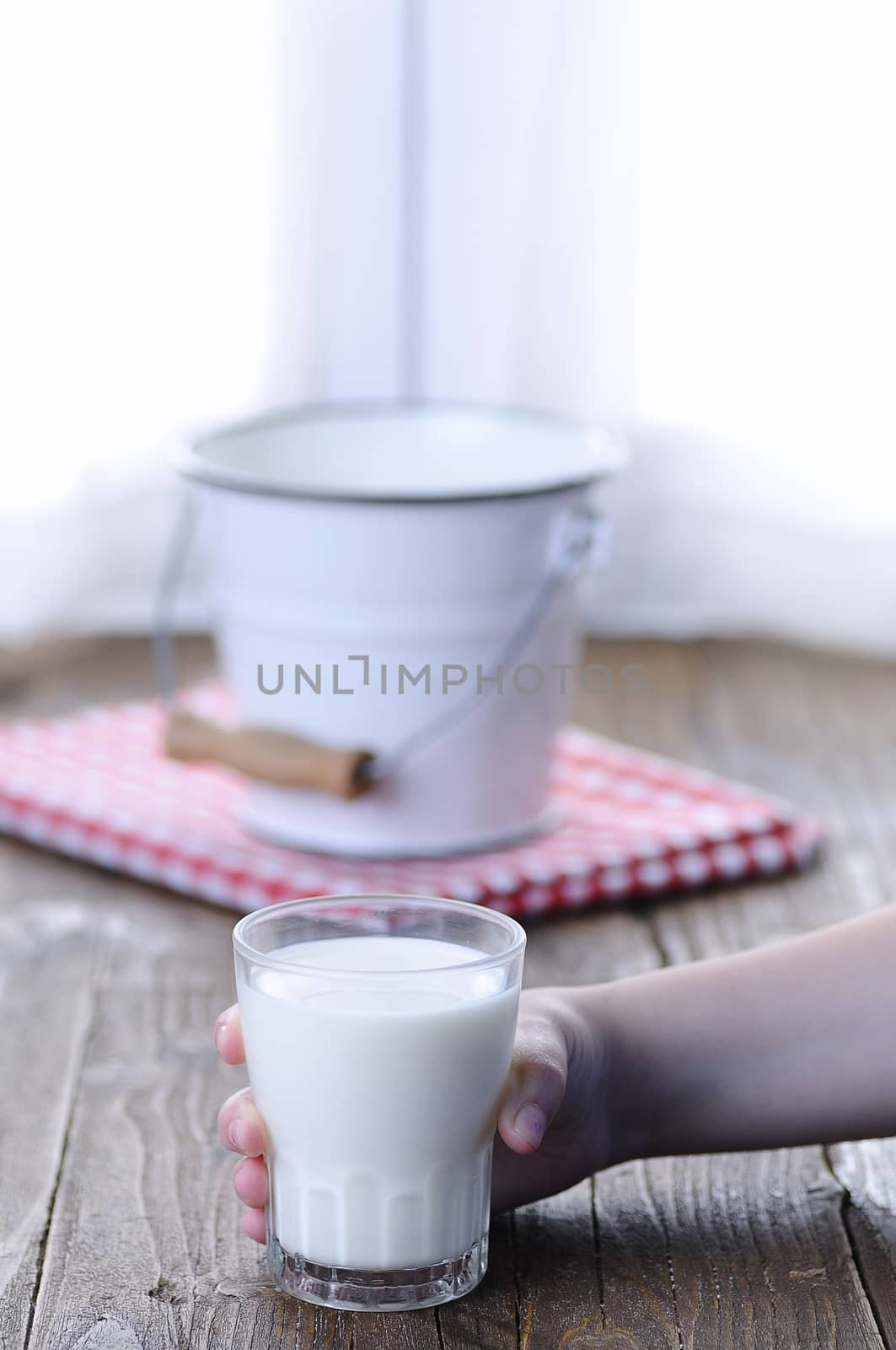 Unrecognizable kid holding glass of fresh tasty milk. Bucket on background.