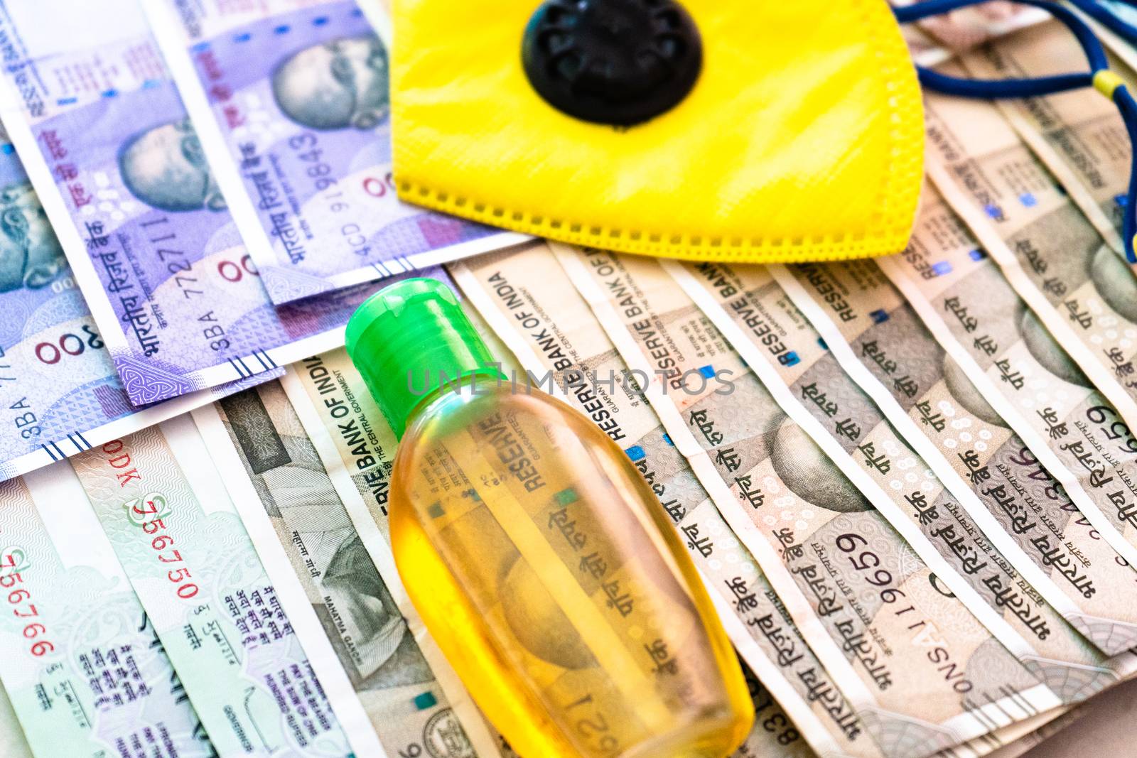 Safety and business essentials yellow mask and sanitizer placed on bed of indian currency. Showing the high price, essentials, large business of manufacturing personal protective essentials or value of health concept