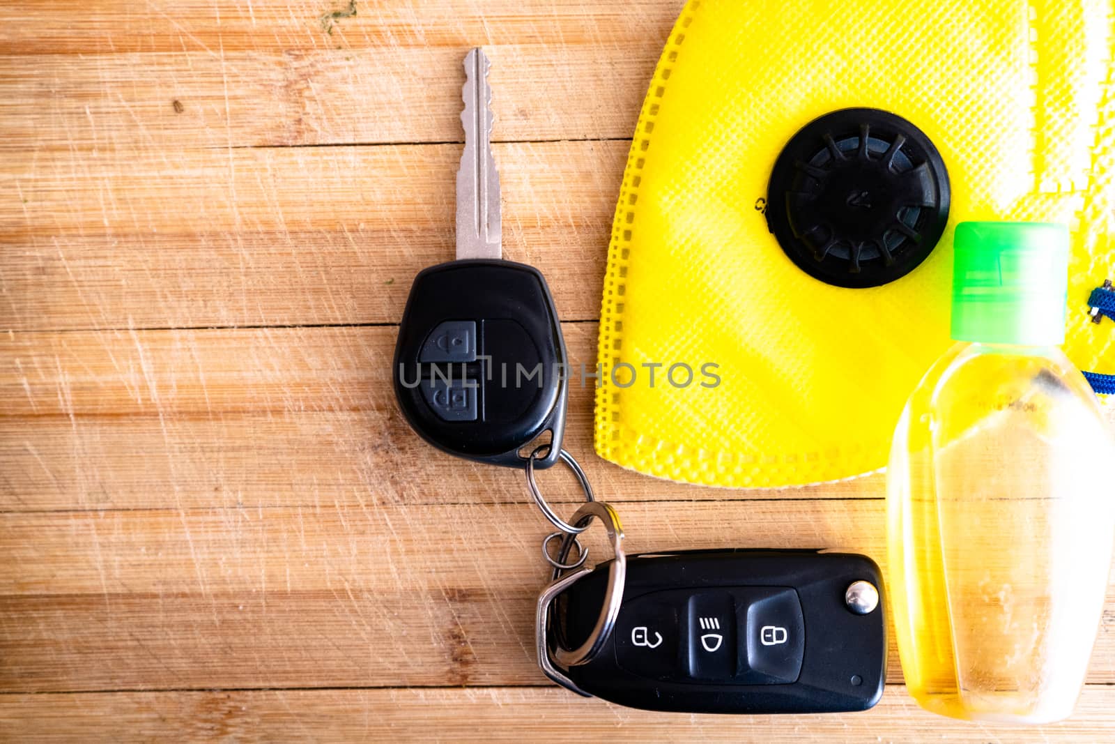 Car keys, sanitizer, yellow mask and more placed on a wooden board with the new essentials for going outdoor with the coronavirus covid 19. Shows necessary safety items for going to office, going shopping to market and more with the new normal