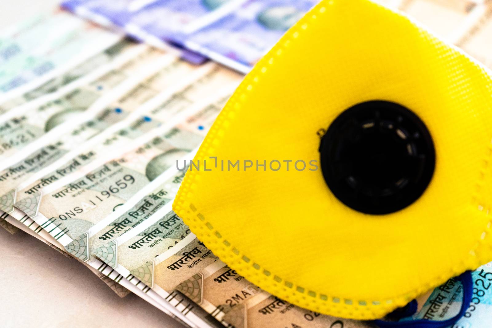 Safety and business essentials yellow mask and sanitizer placed on bed of indian currency. Showing the high price, essentials, large business of manufacturing personal protective essentials or value of health concept