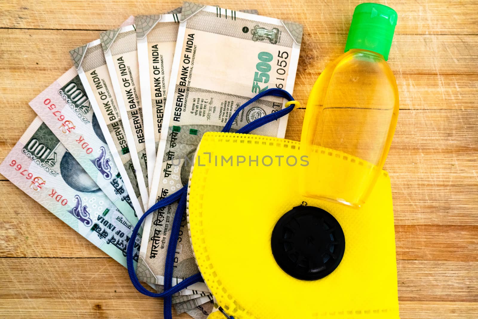 Flatlay with indian currency, yellow N95 face mask, sanitizer and more on a wooden background. Essentials for going out during the coronavirus for safety in the new normal