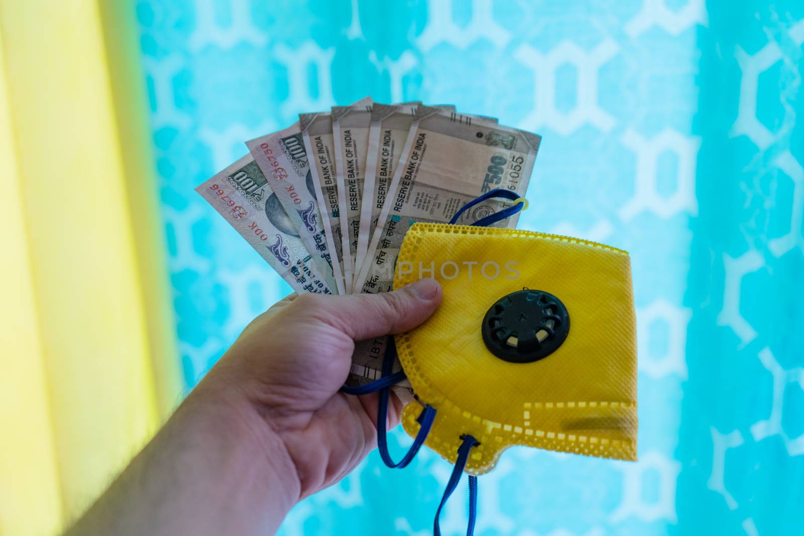 Hand holding out indian currency notes against a colorful background. Showing the essentials for doing business in India with the coronavirus covid19 pandemic and safety requirements