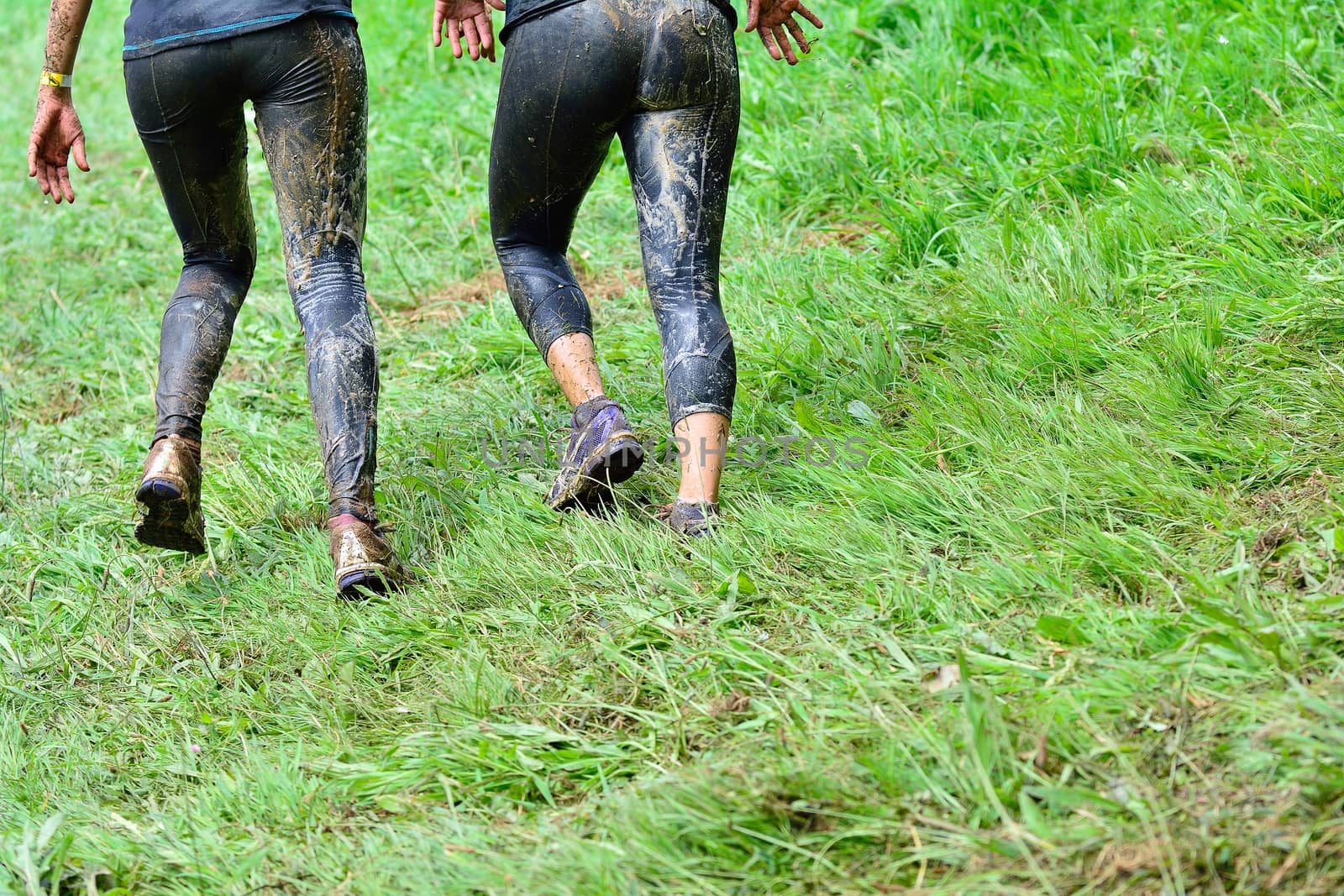 Back view of two unrecognizable sportswomen running in dirty clothes at extreme obstacle race