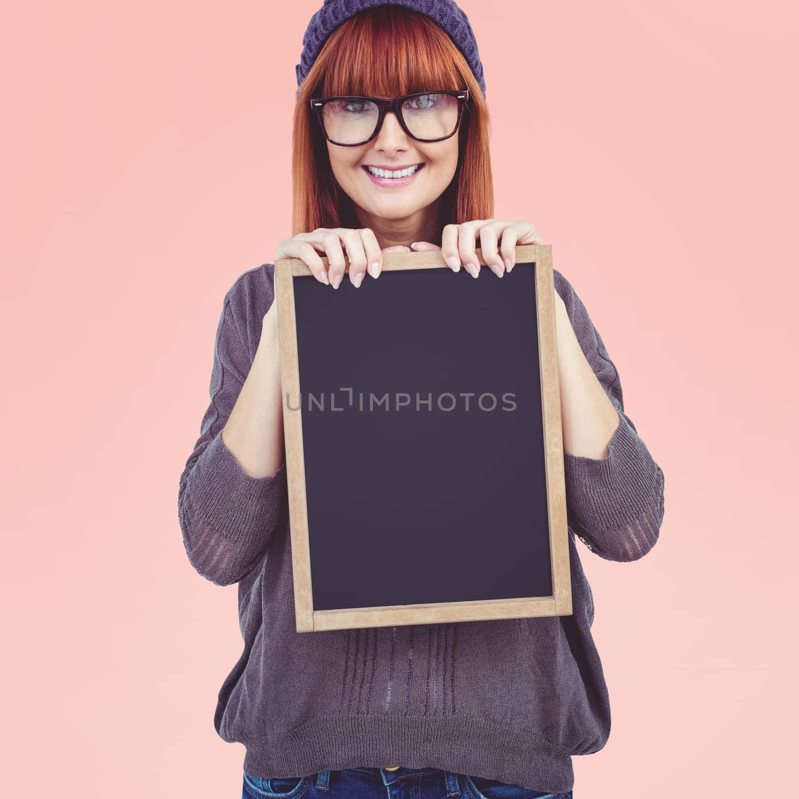 Smiling hipster woman holding blackboard against pastel pink