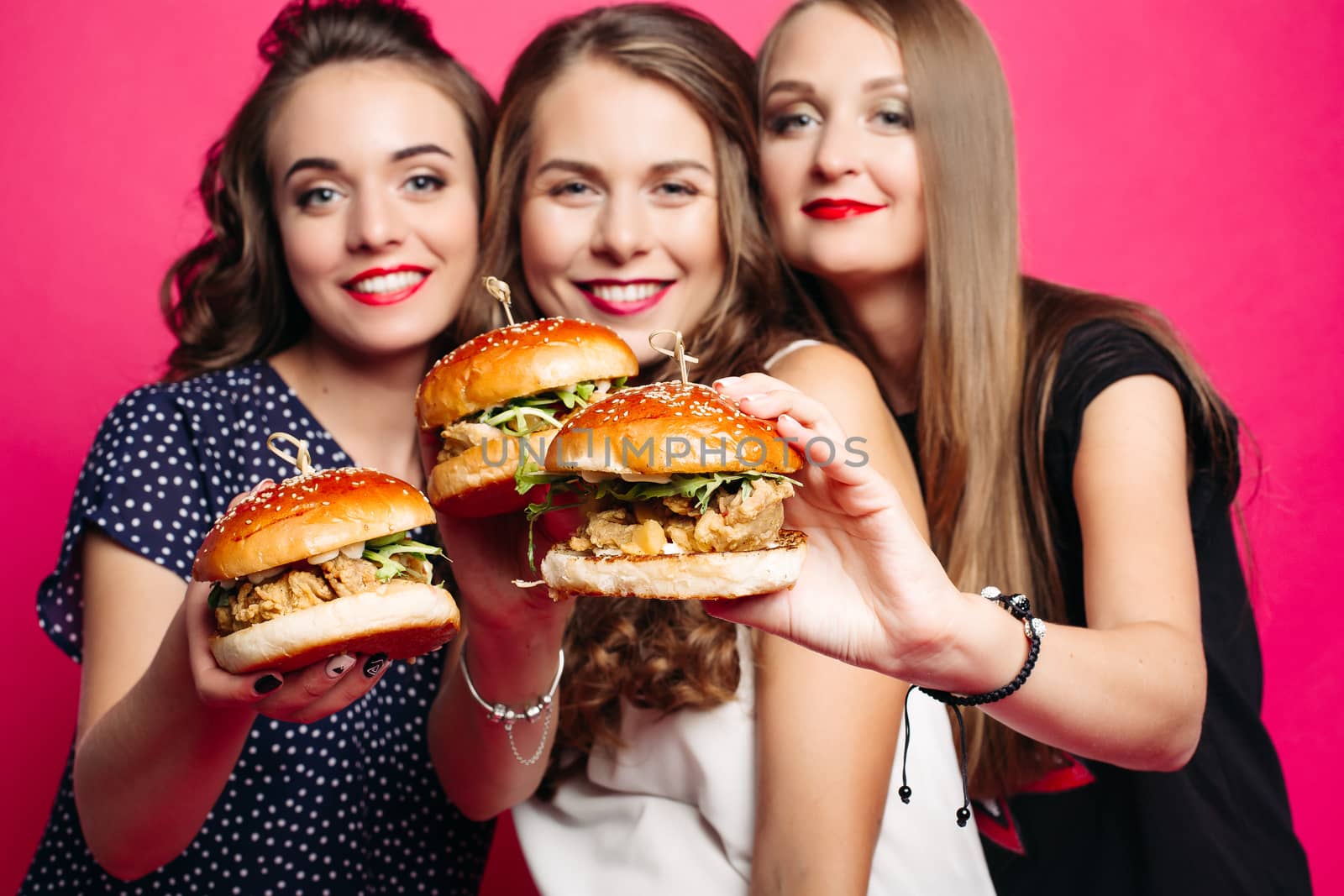 Portrait of beautiful ladies smiling at camera holding juicy delicious burgers in foreground. Fast food concept.